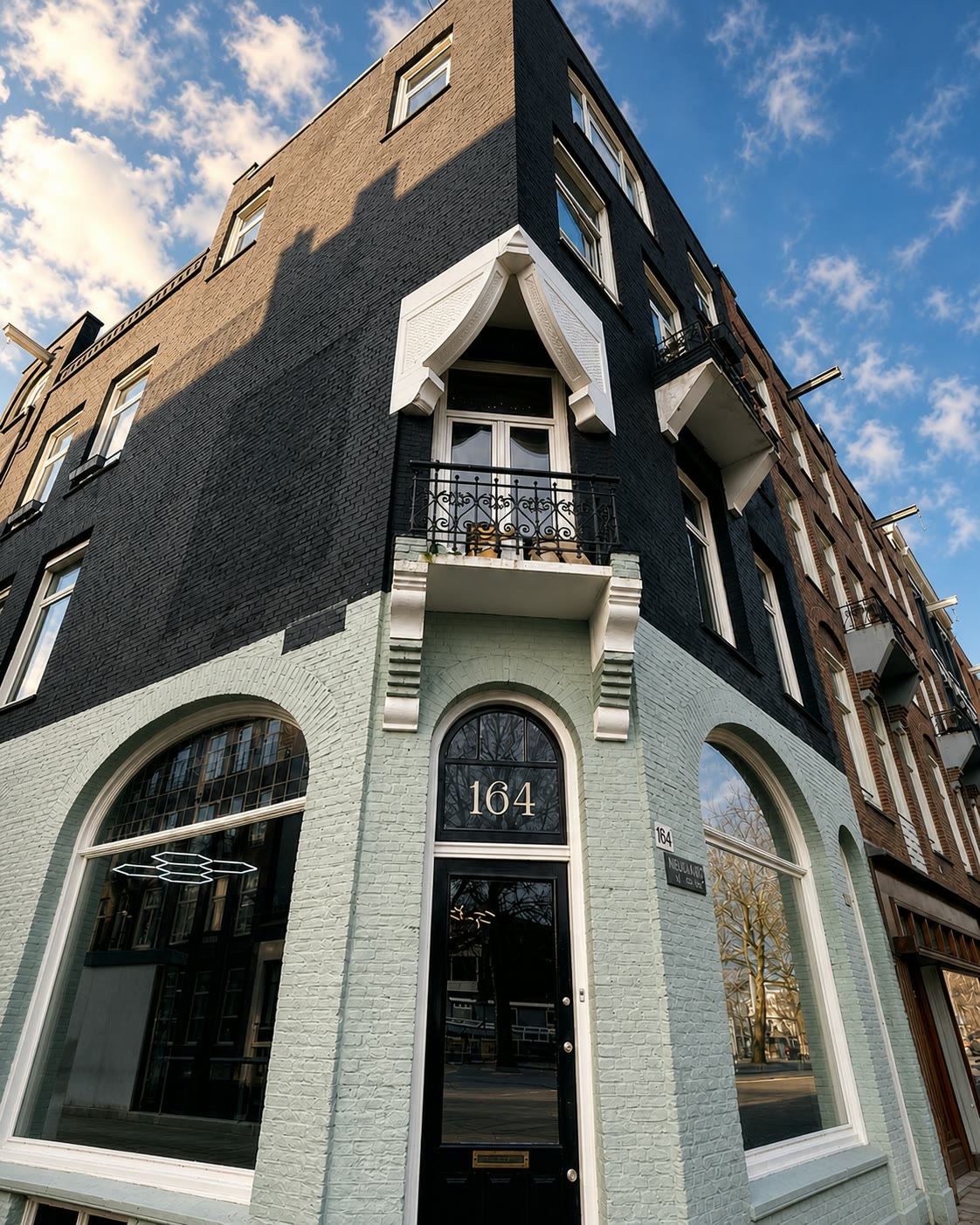 The Empire Barbershop corner building on an Amsterdam street, arched windows and a pale facade under a blue sky.